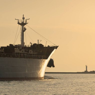 Vinçleri olan büyük bir kargo gemisi gün batımında limandan ayrılıyor. Baltık Denizi. Dramatik fırtına gökyüzü. Yük taşımacılığı, lojistik, küresel iletişim, ekonomi, ticaret, sanayi
