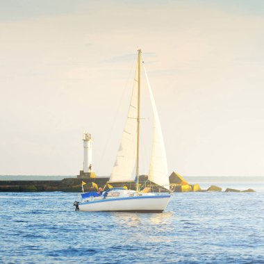 Günbatımında Baltık Denizi 'nde yelkenli yelkenli yelkenli. Fırtınadan sonra açık gökyüzü, yumuşak güneş ışığı. Deniz feneri. Ulaşım, seyahat, gezi, spor, eğlence, boş zaman aktivitesi, yarış, yelkenli yarışı
