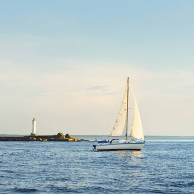 Günbatımında Baltık Denizi 'nde yelkenli yelkenli yelkenli. Fırtınadan sonra açık gökyüzü, yumuşak güneş ışığı. Deniz feneri. Ulaşım, seyahat, gezi, spor, eğlence, boş zaman aktivitesi, yarış, yelkenli yarışı