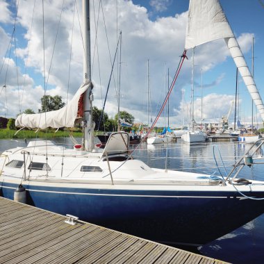 Güneşli bir yaz gününde mavi şalopalı bir yat rıhtıma demirli. Arka planda yelkenliler var. Baltık Denizi, Avrupa. Tatiller, ulaşım, spor, eğlence, turizm, seyahat, balıkçılık, liman hizmeti