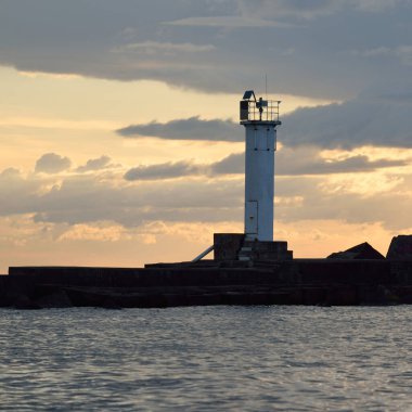 Güneş pilli deniz feneri. Baltık Denizi. Fırtınadan sonra dramatik günbatımı gökyüzü. Parlayan bulutlar, altın güneş ışığı. Umut ve barışın sembolü. Mimarlık, seyahat yerleri, navigasyon, yelkencilik.