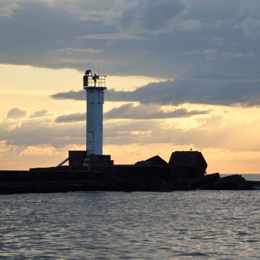 Güneş pilli deniz feneri. Baltık Denizi. Fırtınadan sonra dramatik günbatımı gökyüzü. Parlayan bulutlar, altın güneş ışığı. Umut ve barışın sembolü. Mimarlık, seyahat yerleri, navigasyon, yelkencilik.