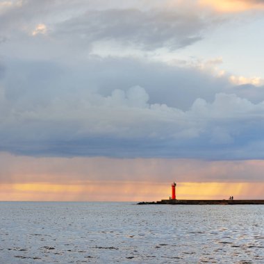 Güneş pilli deniz feneri. Baltık Denizi. Fırtınadan sonra dramatik günbatımı gökyüzü. Parlayan bulutlar, altın güneş ışığı. Umut ve barışın sembolü. Mimarlık, seyahat yerleri, navigasyon, yelkencilik.