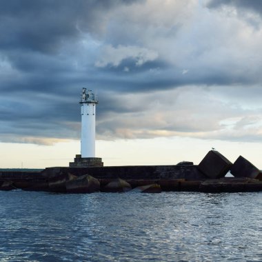 Güneş pilli deniz feneri. Baltık Denizi. Fırtınadan sonra dramatik günbatımı gökyüzü. Parlayan bulutlar, altın güneş ışığı. Umut ve barışın sembolü. Mimarlık, seyahat yerleri, navigasyon, yelkencilik.