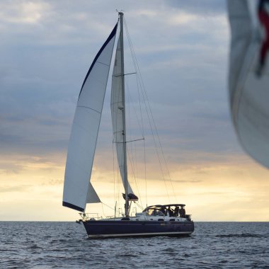 Baltık Denizi 'nde yelkenli bir yat. Gün batımı. Fırtınadan sonra dramatik bir gökyüzü, altın güneş ışığı. Ulaşım, seyahat, gezi, yat yarışı, spor, eğlence, boş zaman aktivitesi, yaşam tarzı