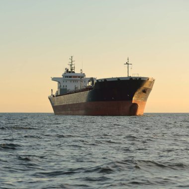 Büyük bir tanker gemisi gün batımında açık denizde hareket ediyor. Altın güneş ışığı. Yük taşımacılığı, yakıt ve enerji üretimi, denizcilik gemisi, lojistik, küresel iletişim, ekonomi, ticaret, sanayi