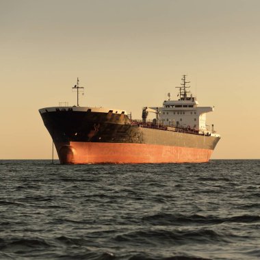 Büyük bir kargo gemisi (kimyasal tanker, 184 metre uzunluğunda) gün batımında açık denizde yol alır. Altın güneş ışığı. Yük taşımacılığı, yakıt, enerji üretimi, denizcilik gemisi, lojistik, ekonomi, sanayi