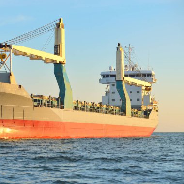 Büyük vinç gemisi (genel yük, 146 metre uzunluğunda) gün batımında açık denizde yol alır. Altın güneş ışığı. Yük taşımacılığı, lojistik, küresel iletişim, ekonomi, sanayi, dünya çapında taşımacılık