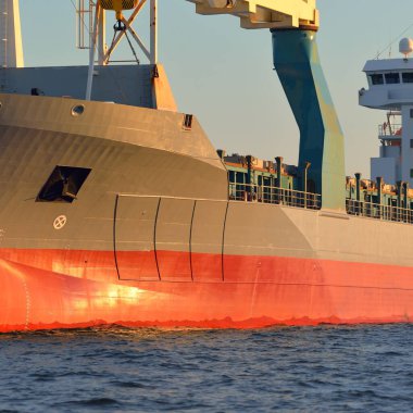 Büyük vinç gemisi (genel yük, 146 metre uzunluğunda) gün batımında açık denizde yol alır. Altın güneş ışığı. Yük taşımacılığı, lojistik, küresel iletişim, ekonomi, sanayi, dünya çapında taşımacılık