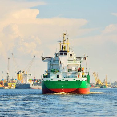 Büyük yeşil yük gemisi gün batımında kargo terminaline varacak. Arka planda gemiler ve vinçler var. Dramatik bulut manzarası. Yük taşımacılığı, küresel iletişim, endüstri, ekonomi, lojistik