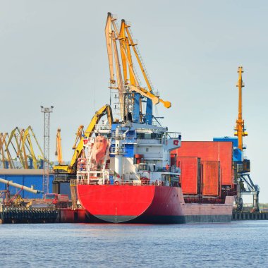 Liman terminalinde büyük bir kargo gemisi yükleniyor, arka planda vinçler var. Yük taşımacılığı, lojistik, küresel iletişim, ekonomi, ticaret, sanayi, özel ekipman