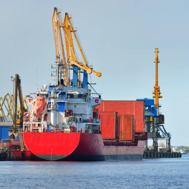 Liman terminalinde büyük bir kargo gemisi yükleniyor, arka planda vinçler var. Yük taşımacılığı, lojistik, küresel iletişim, ekonomi, ticaret, sanayi, özel ekipman