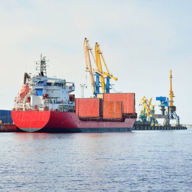 Liman terminalinde büyük bir kargo gemisi yükleniyor, arka planda vinçler var. Yük taşımacılığı, lojistik, küresel iletişim, ekonomi, ticaret, sanayi, özel ekipman