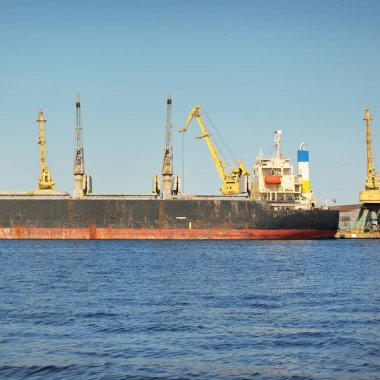 İskele terminalinden yüklenen büyük eski bir kargo gemisi, arka planda vinçler. Yük taşımacılığı, lojistik, küresel iletişim, ekonomi, ticaret, sanayi