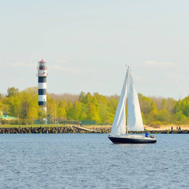 Günbatımında Baltık Denizi 'nde yelkenli yelkenli yelkenli. Fırtınadan sonra açık gökyüzü, yumuşak güneş ışığı. Deniz feneri. Ulaşım, seyahat, gezi, spor, eğlence, boş zaman aktivitesi, yarış, yelkenli yarışı