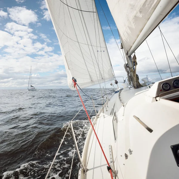 Açık bir günde açık denizde yelken açan beyaz yelkenli bir yat. Güverteden pruvaya bir manzara. Kümülüs bulutları. Ulaşım, seyahat, gezi, spor, eğlence, boş zaman aktivitesi, yarış, yelkenli yarışı