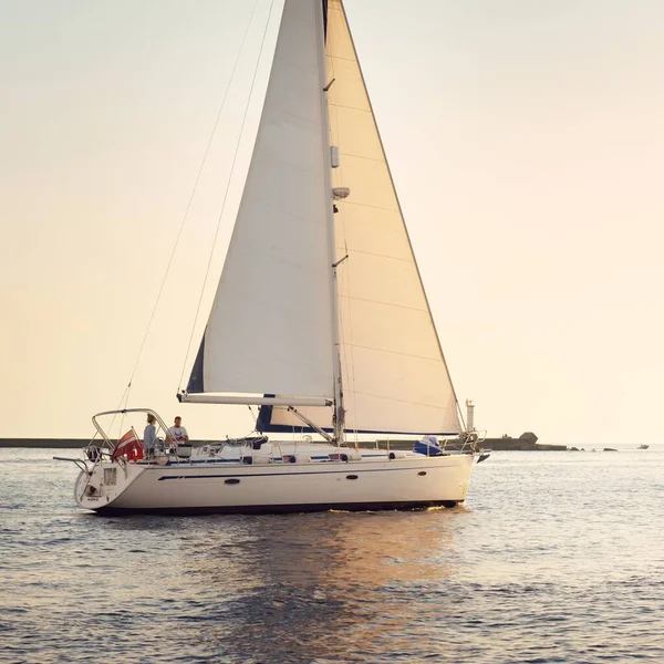 White sloop rigged yacht sailing in the Baltic sea at sunset. Clear sky after the storm, golden sunlight. Transportation, travel, cruise, sport, recreation, leisure activity, racing, regatta