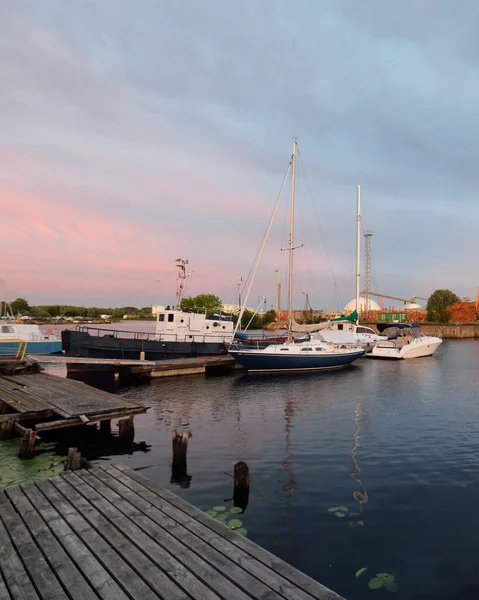 Old tugboat and blue sloop rigged sailboat moored to a pier in a yacht marina at sunset. Dramatic sky. Vacations, transportation, sport, recreation, tourism, cruise, fishing, port service