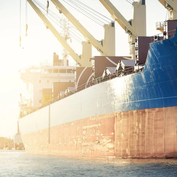 Liman terminalinde büyük bir kargo gemisi yükleniyor, arka planda vinçler var. Yük taşımacılığı, deniz taşımacılığı, lojistik, küresel iletişim, dünya çapında taşımacılık, ekonomi, ticaret, sanayi