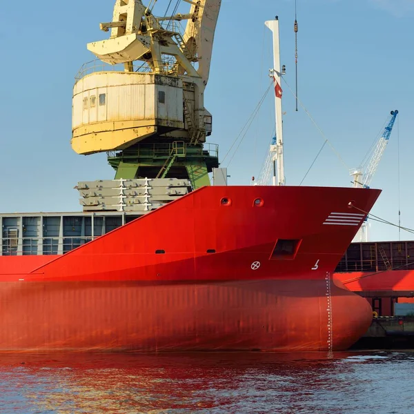 Red ship (general cargo, 89 meters length) loading in port terminal, cranes in the background. Freight transportation, logistics, global communications, worldwide shipping, economy, business, industry