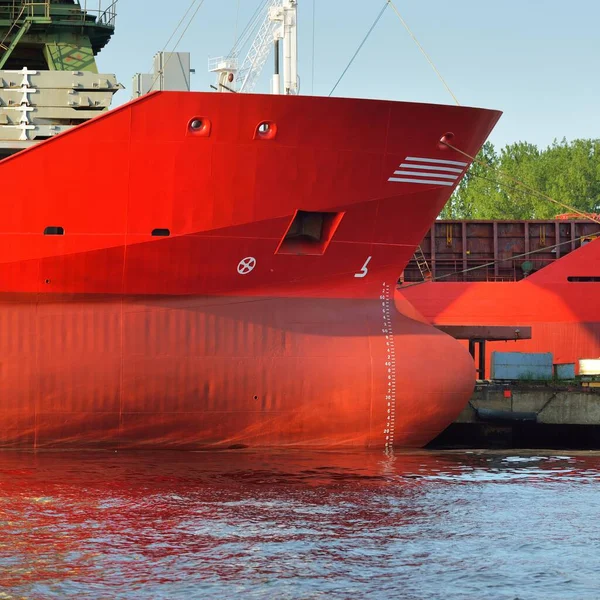 Red ship (general cargo, 89 meters length) loading in port terminal, cranes in the background. Freight transportation, logistics, global communications, worldwide shipping, economy, business, industry