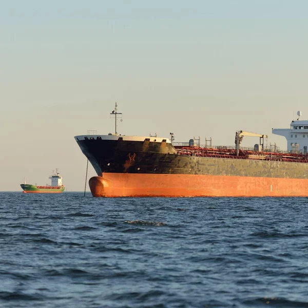 Large cargo ship (chemical tanker, 184 meters length) sailing in an open sea at sunset. Golden sunlight. Freight transportation, fuel, power generation, nautical vessel, logistics, economy, industry