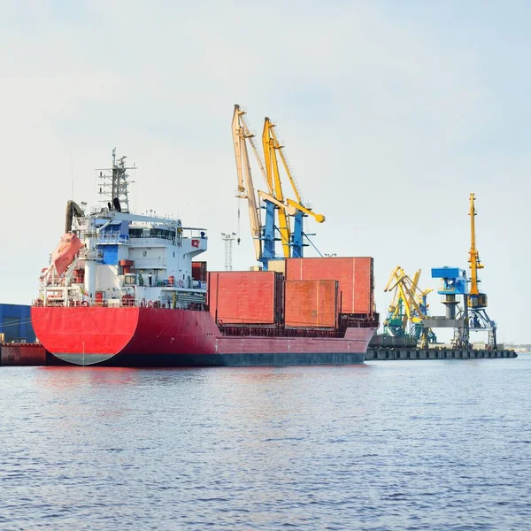 Liman terminalinde büyük bir kargo gemisi yükleniyor, arka planda vinçler var. Yük taşımacılığı, lojistik, küresel iletişim, ekonomi, ticaret, sanayi, özel ekipman