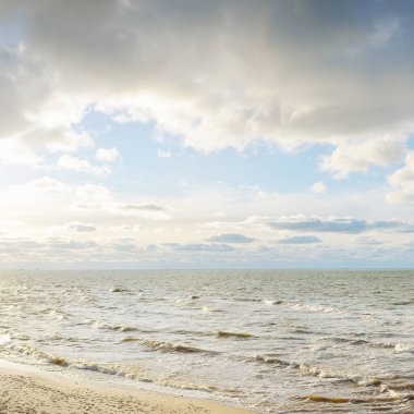 Kumlu bir sahilden (kum tepeleri) Baltık denizinin panoramik görüntüsü. Parlayan bulutlarla, dalgalarla ve su sıçramalarıyla berrak bir gökyüzü. Idyllic deniz manzarası. Sıcak kış havası, iklim değişikliği, doğa