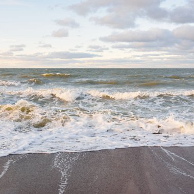 Gün batımında Baltık kıyıları (kum tepeleri). Yumuşak güneş ışığı, parlayan bulutlar, dalgalar ve su fışkıran berrak gökyüzü. Idyllic deniz manzarası. Liepaja, Letonya, Avrupa. Sıcak kış havası, iklim değişikliği, doğa
