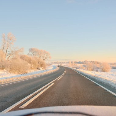 Karla kaplı orman ve kırsal alanda boş otoyol (asfalt yol). Gündoğumu, kar yağışı. Avrupa. Doğa, Noel tatilleri, uzak yerler, kış lastikleri, tehlikeli sürüş konsepti