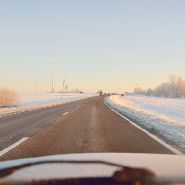 Karla kaplı orman ve kırsal alanda boş otoyol (asfalt yol). Gündoğumu, kar yağışı. Avrupa. Doğa, Noel tatilleri, uzak yerler, kış lastikleri, tehlikeli sürüş konsepti