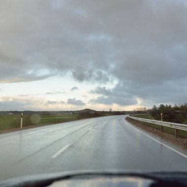 Gün batımında tarla ve orman boyunca asfalt yol (karayolu). Arabadan görüntü. Turizm, tatiller, uzak yerler, lojistik kavramlar