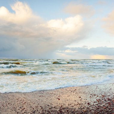 Fırtınadan sonra Baltık Denizi. Dramatik gökyüzü, parlayan bulutlar, yumuşak güneş ışığı. Dalgalar, su sıçratma. Resimli manzara, deniz manzarası, doğa. Panoramik görünüm