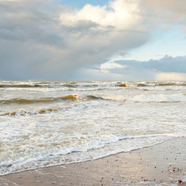 Fırtınadan sonra Baltık Denizi. Dramatik gökyüzü, parlayan bulutlar, yumuşak güneş ışığı. Dalgalar, su sıçratma. Resimli manzara, deniz manzarası, doğa. Panoramik görünüm