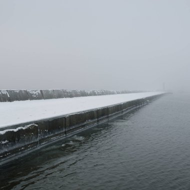 Kumlu sahilden Baltık Denizi 'nin panoramik manzarası. Deniz fenerine dolaş, dalgalar. Yoğun beyaz sis, sis, kar. Dalgalar, su sıçramaları. Deniz Burnu. Tek renkli kış manzarası