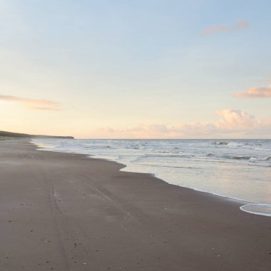 Gün batımında Baltık kıyıları (kum tepeleri). Yumuşak güneş ışığı, parlayan bulutlar, dalgalar ve su fışkıran berrak gökyüzü. Idyllic deniz manzarası. Liepaja, Letonya, Avrupa. Sıcak kış havası, iklim değişikliği, doğa