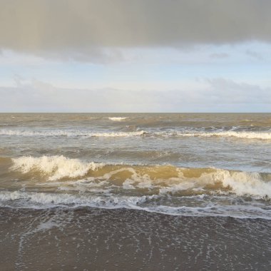 Kumlu bir sahilden (kum tepeleri) Baltık denizinin panoramik görüntüsü. Koyu bulutlu dramatik bir gökyüzü. Dalgalar, su sıçramaları. Idyllic deniz manzarası. Sıcak kış havası, iklim değişikliği, doğa. Danimarka