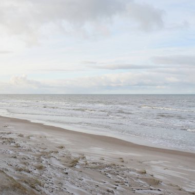 Kumlu bir sahilden (kum tepeleri) Baltık denizinin panoramik görüntüsü. Koyu bulutlu dramatik bir gökyüzü. Dalgalar, su sıçramaları. Idyllic deniz manzarası. Sıcak kış havası, iklim değişikliği, doğa. Danimarka