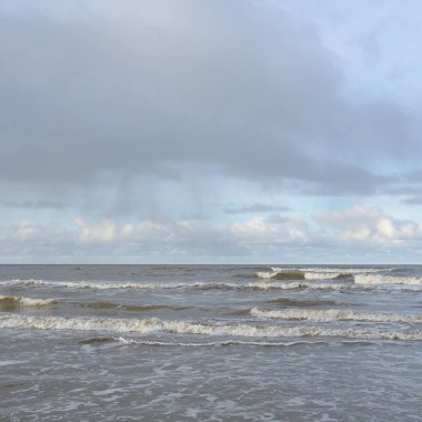 Kumlu bir sahilden (kum tepeleri) Baltık denizinin panoramik görüntüsü. Koyu bulutlu dramatik bir gökyüzü. Dalgalar, su sıçramaları. Idyllic deniz manzarası. Sıcak kış havası, iklim değişikliği, doğa. Danimarka