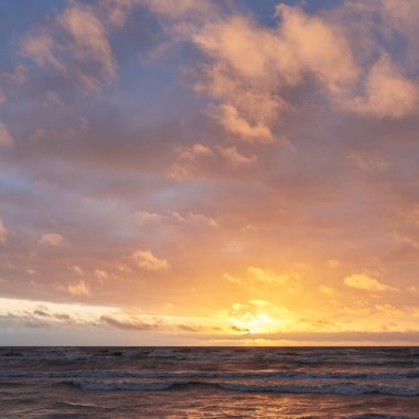 Fırtınadan sonra gün batımında Baltık Denizi. Dramatik gökyüzü, parlayan bulutlar, dofty altın güneş ışığı, dalgalar, fışkıran su. Resimli panoramik manzara. Doğa, çevre, ekoloji