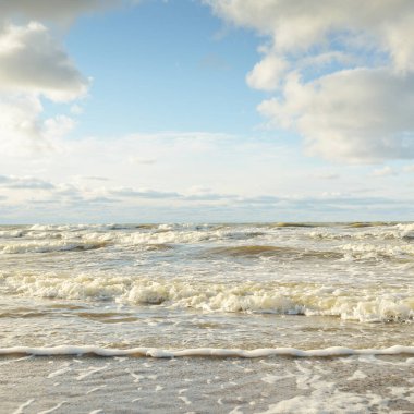 Kumlu bir sahilden (kum tepeleri) Baltık denizinin panoramik görüntüsü. Parlayan bulutlarla, dalgalarla ve su sıçramalarıyla berrak bir gökyüzü. Idyllic deniz manzarası. Sıcak kış havası, iklim değişikliği, doğa