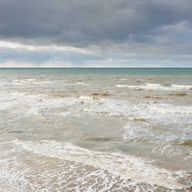 Kumlu bir sahilden (kum tepeleri) Baltık denizinin panoramik görüntüsü. Parlayan bulutlarla, dalgalarla ve su sıçramalarıyla berrak bir gökyüzü. Idyllic deniz manzarası. Sıcak kış havası, iklim değişikliği, doğa