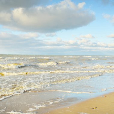 Kumlu bir sahilden (kum tepeleri) Baltık denizinin panoramik görüntüsü. Parlayan bulutlarla, dalgalarla ve su sıçramalarıyla berrak bir gökyüzü. Idyllic deniz manzarası. Sıcak kış havası, iklim değişikliği, doğa