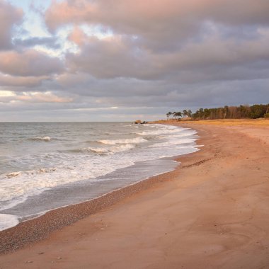 Gün batımında Baltık kıyıları (kum tepeleri). Yumuşak güneş ışığı, parlayan bulutlar, dalgalar ve su fışkıran berrak gökyüzü. Idyllic deniz manzarası. Liepaja, Letonya, Avrupa. Sıcak kış havası, iklim değişikliği, doğa