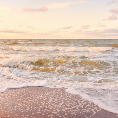 Gün batımında Baltık kıyıları (kum tepeleri). Yumuşak güneş ışığı, parlayan bulutlar, dalgalar ve su fışkıran berrak gökyüzü. Idyllic deniz manzarası. Liepaja, Letonya, Avrupa. Sıcak kış havası, iklim değişikliği, doğa
