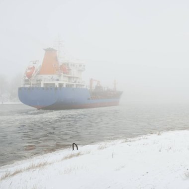 Donmuş nehir, büyük bir kargo gemisi. Kar, kalın sis. Kış kentsel manzarası kavramı. Ulaşım, denizcilik gemisi, küresel iletişim, endüstri, lojistik