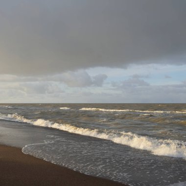 Gün batımında Baltık kıyıları (kum tepeleri). Yumuşak güneş ışığı, parlayan bulutlar, dalgalar ve su fışkıran berrak gökyüzü. Idyllic deniz manzarası. Liepaja, Letonya, Avrupa. Sıcak kış havası, iklim değişikliği, doğa
