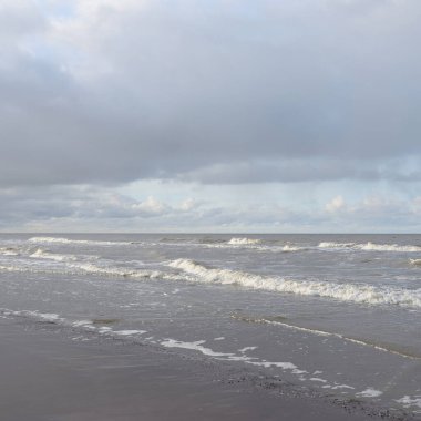 Kumlu bir sahilden (kum tepeleri) Baltık denizinin panoramik görüntüsü. Koyu bulutlu dramatik bir gökyüzü. Dalgalar, su sıçramaları. Idyllic deniz manzarası. Sıcak kış havası, iklim değişikliği, doğa. Danimarka