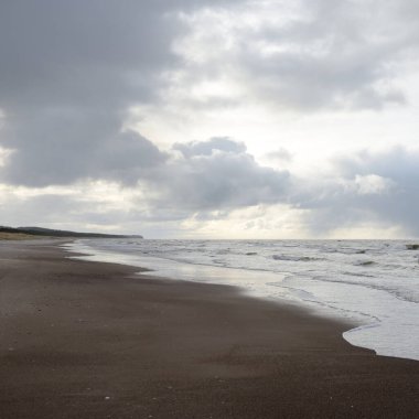 Gün batımında Baltık kıyıları (kum tepeleri). Yumuşak güneş ışığı, parlayan bulutlar, dalgalar ve su fışkıran berrak gökyüzü. Idyllic deniz manzarası. Liepaja, Letonya, Avrupa. Sıcak kış havası, iklim değişikliği, doğa