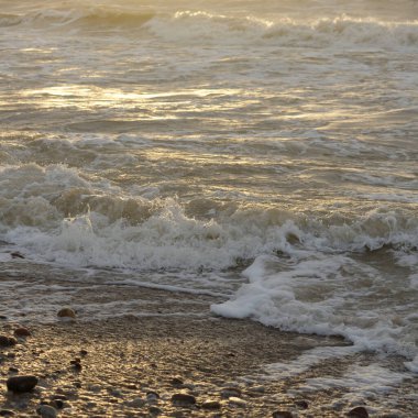 Fırtınadan sonra Baltık kıyıları. Gün batımı, yumuşak güneş ışığı. Su yüzeyi dokusu, çarpan dalgalar, sıçramalar, köpük. Resimli panoramik manzara. Idyllic deniz manzarası. Doğa, çevre, ekoloji temaları
